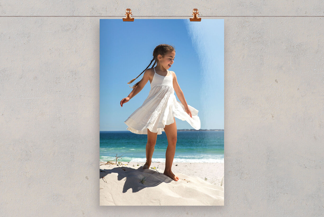 Ein Kind in einem weißen Kleid steht freudig auf einem Sanddüne am Strand und genießt den Sonnenschein.