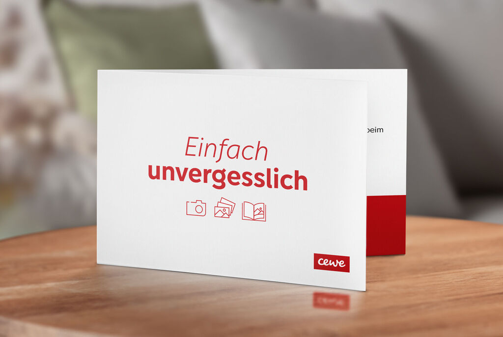 Weiße Grußkarte mit rotem Text "Einfach unvergesslich" auf einem Holztisch.