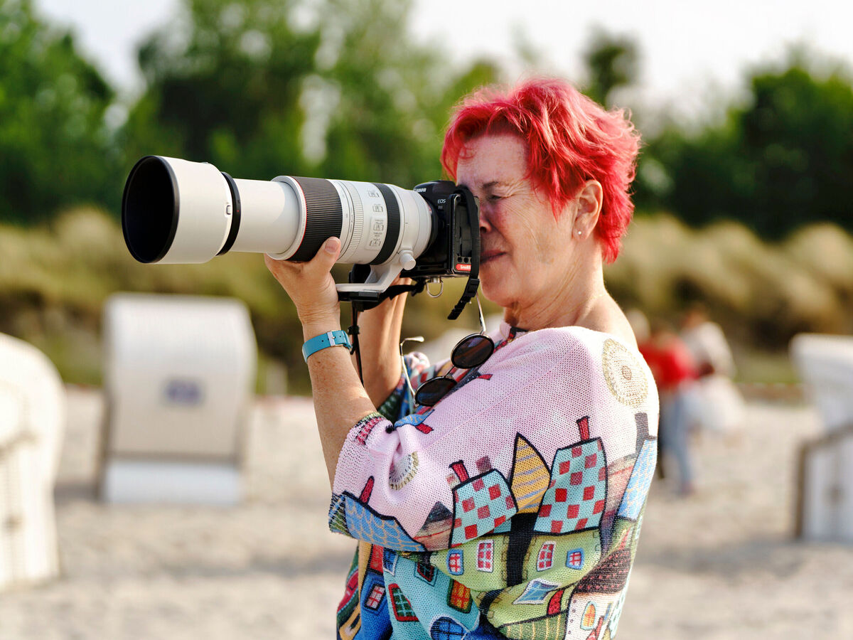 Eine Frau fotografiert am Strand mit einer professionellen Kamera.