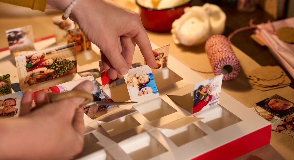 Hände schneiden Fotos von einem Adventskalender ab. Drumherum liegen Bastelutensilien