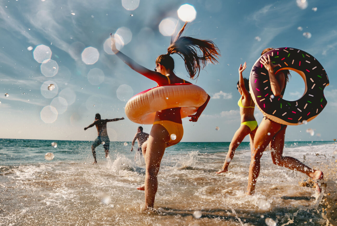 Gruppe läuft in Badekleidung und mit Schwimmringen in die Brandung.