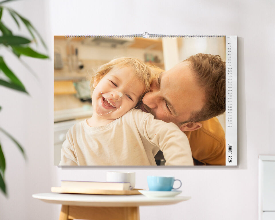 CEWE Fotokalender mit einem Familienfoto hängt an einer hellen Wand über einem Tisch mit Tasse und Dekoration