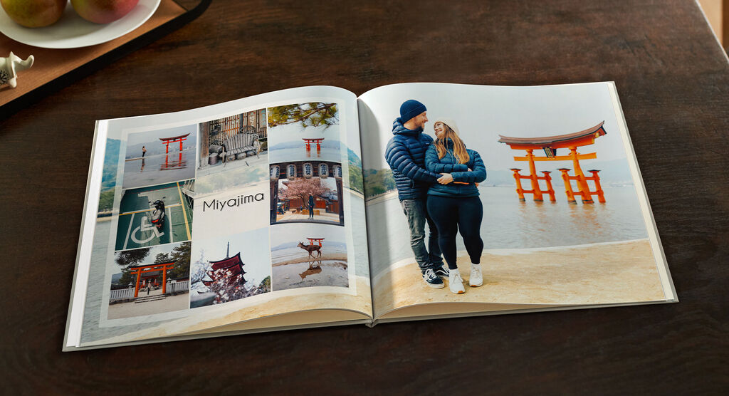 Ein geöffnetes Fotobuch zeigt liebevolle Erinnerungen an einen Urlaub in Miyajima, mit Fotos von roten Torii und einem Paar, das glücklich gemeinsam posiert.