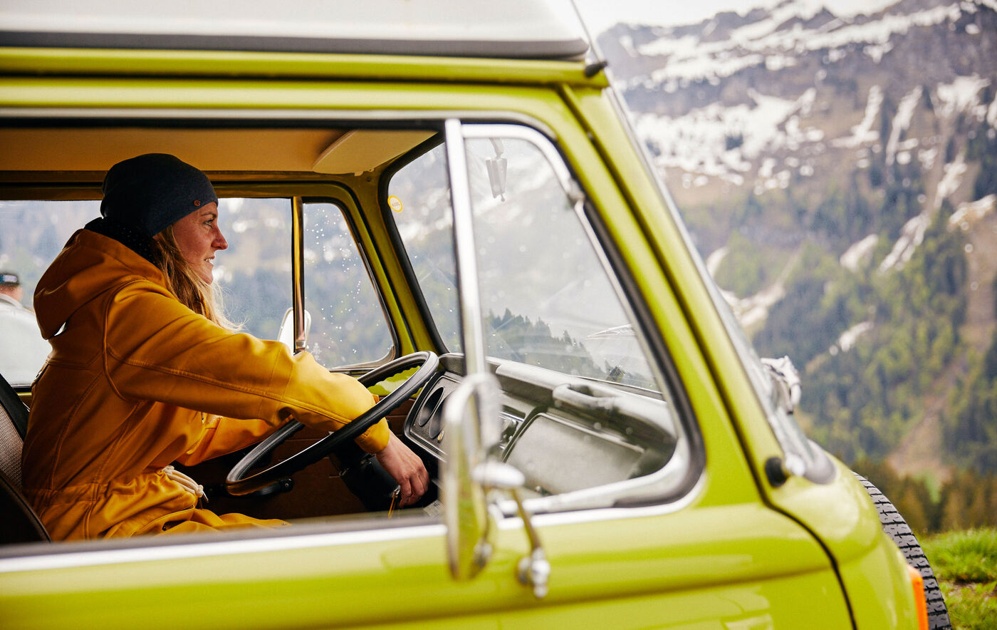 Eine Person sitzt in einem gelben Fahrzeug und genießt die Aussicht auf eine schöne, bergige Landschaft mit schneebedeckten Gipfeln im Hintergrund
