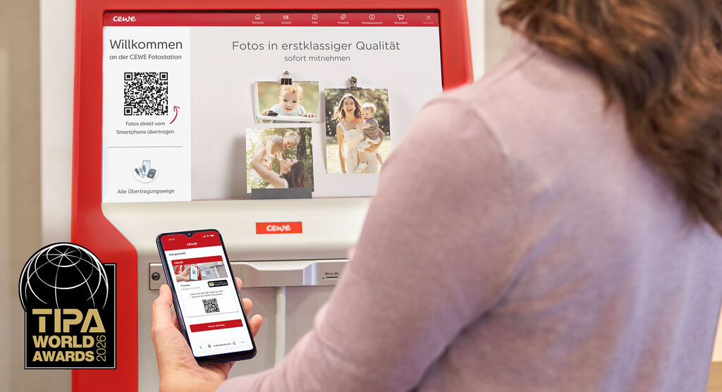 Person steht an einer CEWE Fotostation, hält ein Smartphone mit QR Code und wählt Fotos zur sofortigen Mitnahme aus