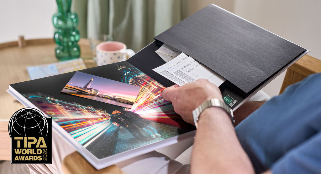CEWE FOTOBUCH liegt auf einem Tisch, eine Person blättert durch Seiten mit Fotos, TIPA World Awards Logo links unten