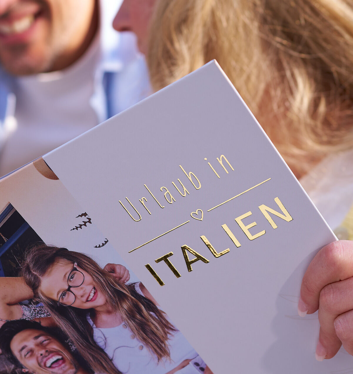 Person hält ein Fotobuch mit der goldenen Aufschrift „Urlaub in Italien“.