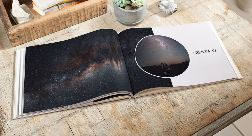 Ein geöffnetes Fotobuch mit einer Nachtaufnahme der Milchstraße und einem Bild von zwei Personen unter dem Sternenhimmel