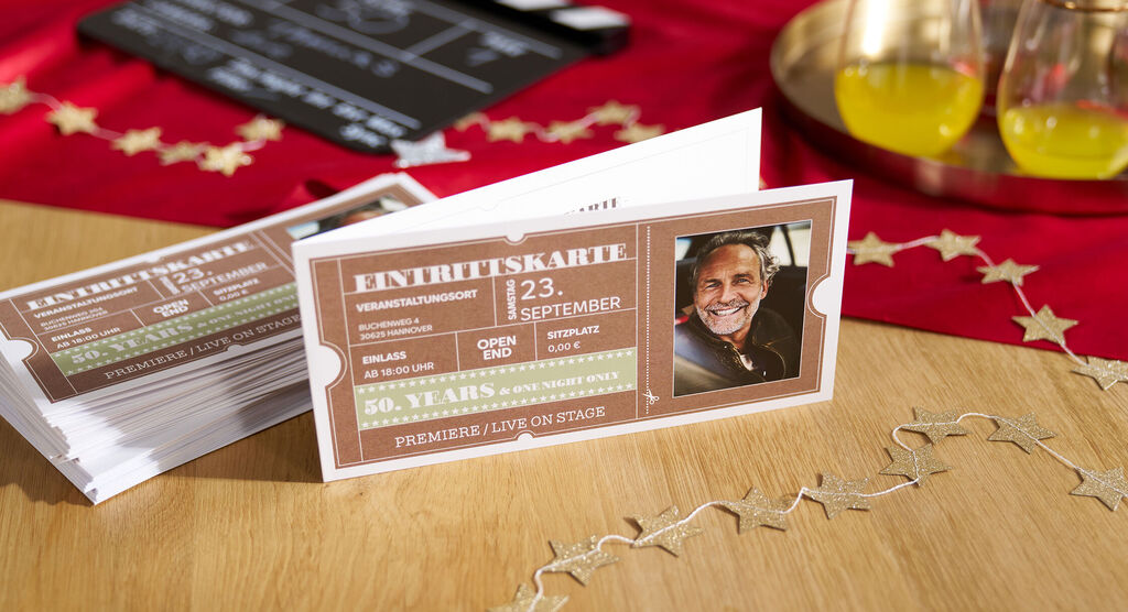Auf einem feierlich geschmückten Tisch liegen personalisierte Einladungskarten in der Optik von Eintrittskarten.