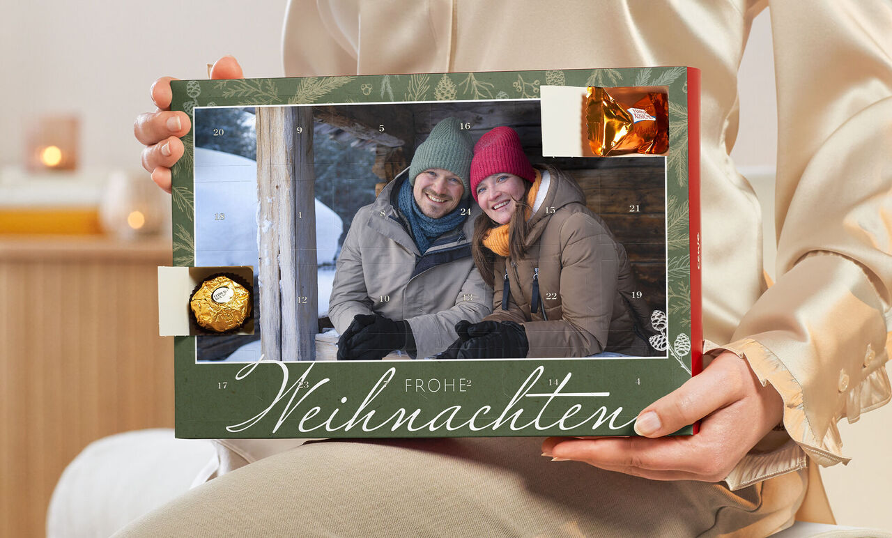 Person hält einen weihnachtlichen Fotokalender mit Schokolade, frohe Stimmung, winterliche Umgebung