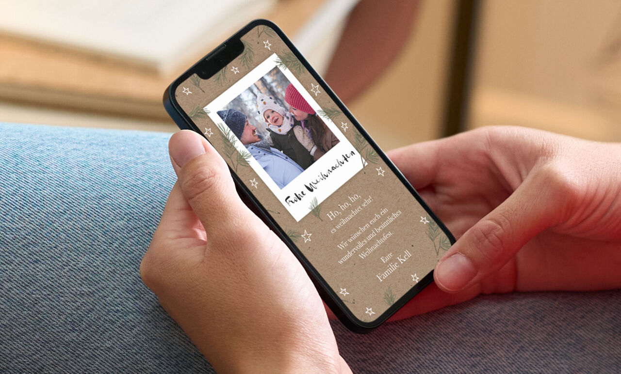 Person hält Smartphone mit CEWE Grußkarte im Weihnachtsdesign und fröhlichem Familienfoto