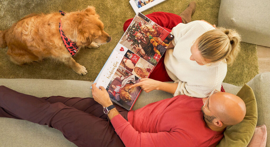 Weihnachtliche Fotoseiten im CEWE FOTOBUCH werden gemeinsam mit Hund angeschaut.