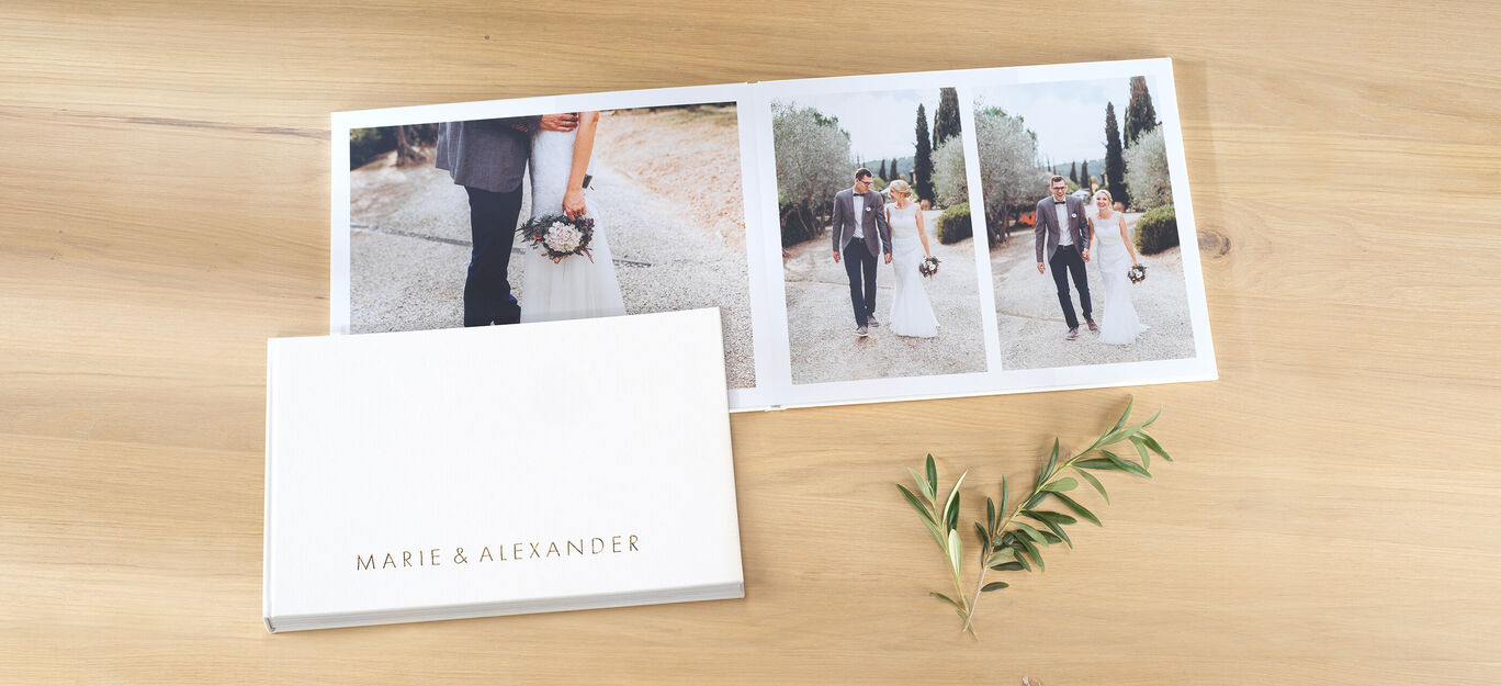 Elegantes CEWE FOTOBUCH mit Bildern von einer Hochzeitsfeier und einer Blume daneben.