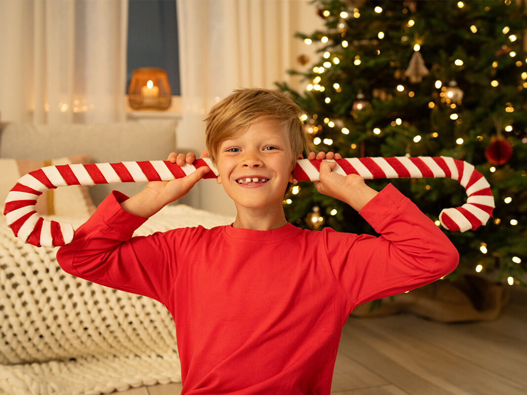 Ein fröhliches Kind hält einen großen Zuckerstangen-Stab in der Weihnachtszeit.