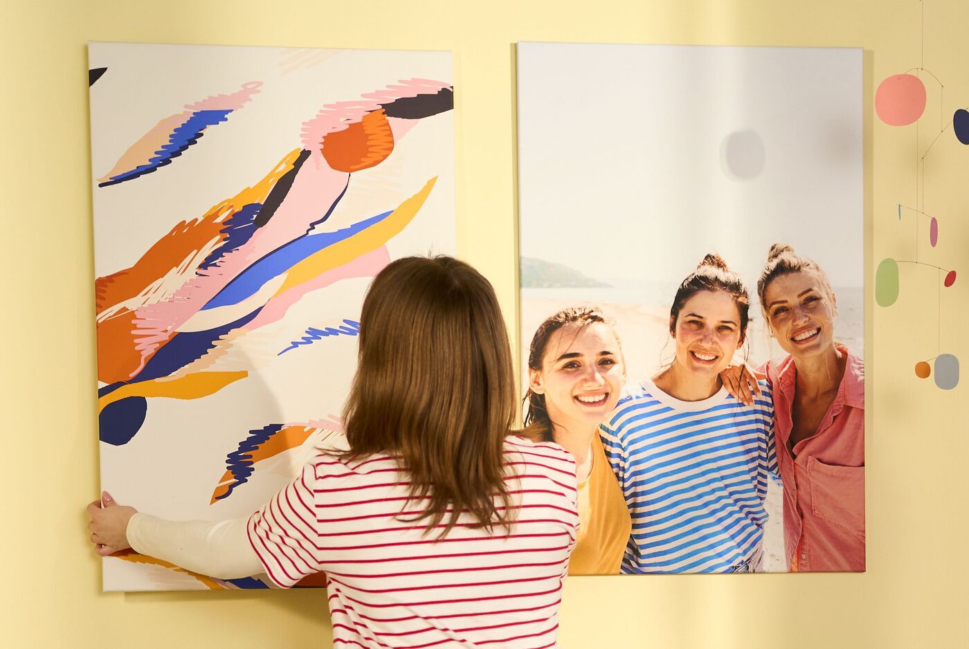 Person hängt personalisiertes CEWE Wandbild mit buntem Design neben ein weiteres Wandbild mit Urlaubsfoto auf