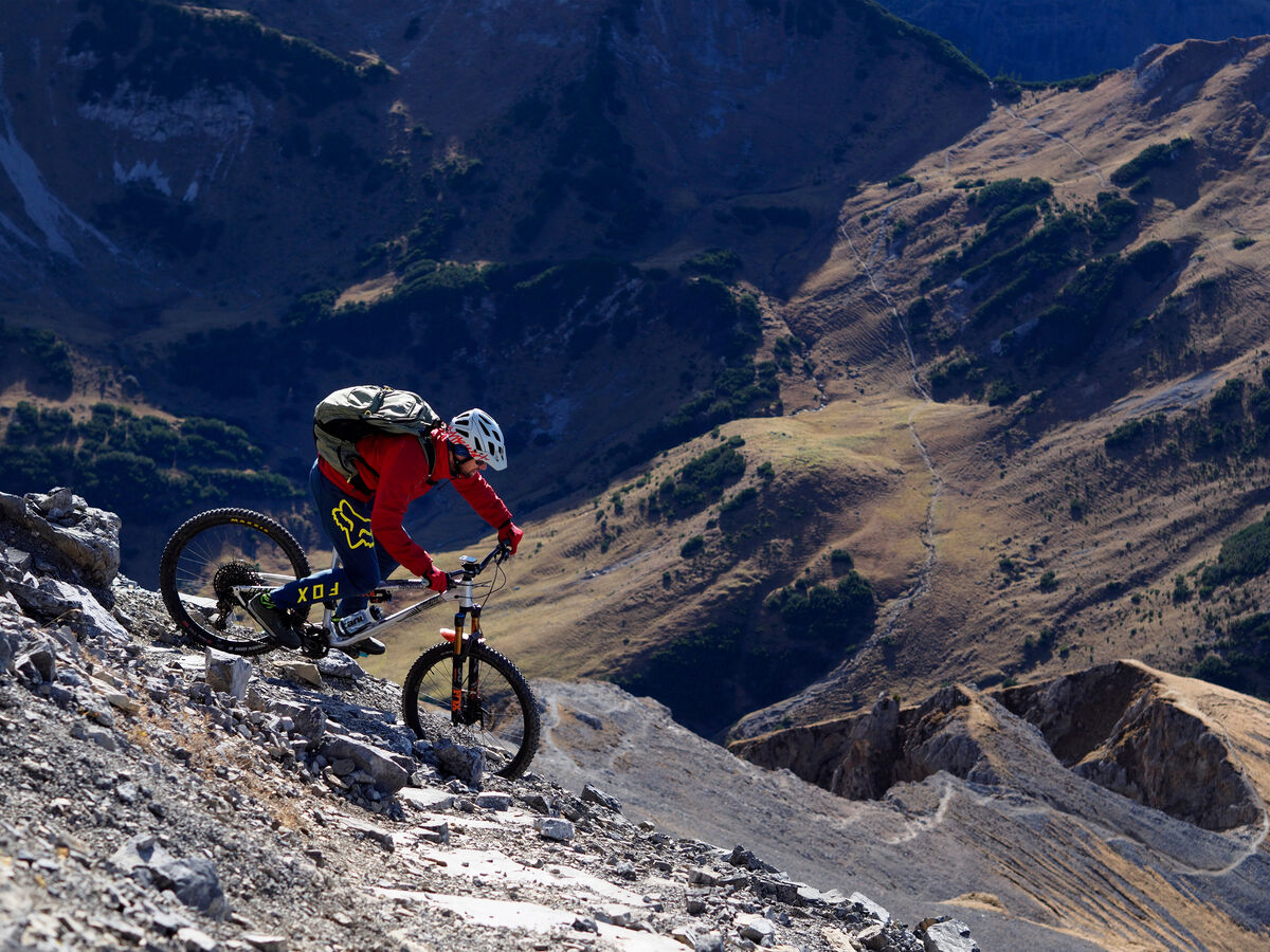 Mountainbiker fährt einen steilen Bergpfad mit Berglandschaft im Hintergrund