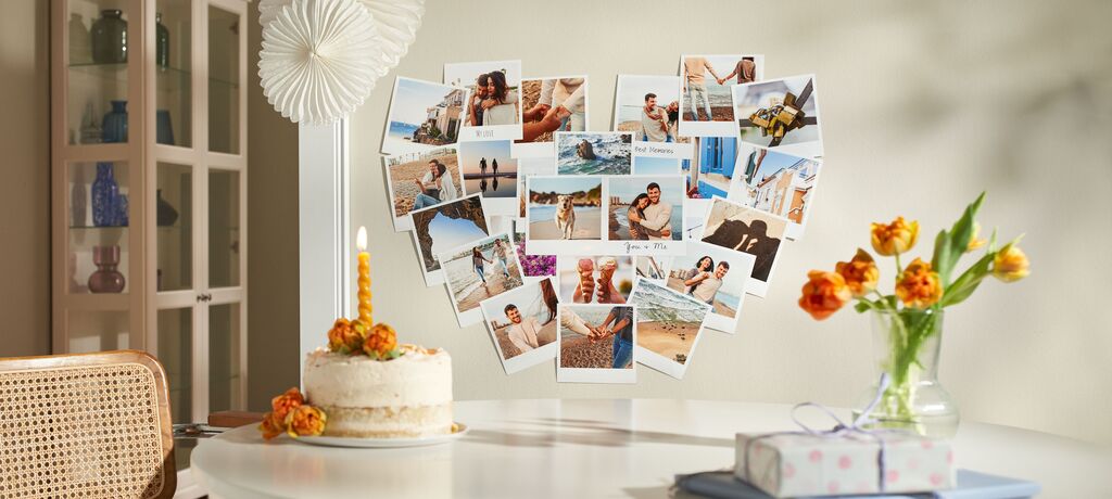 Ein heller Tisch mit einer Torte, Blumen und Fotos von glücklichen Momenten, die an der Wand hängen