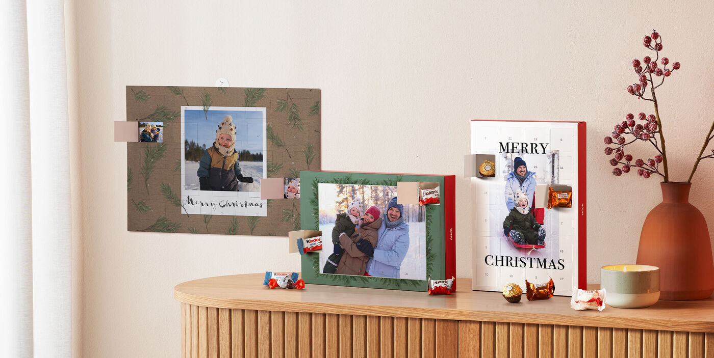 Drei personalisierte Adventskalender mit Fotos und Schokolade auf Sideboard mit winterlicher Deko