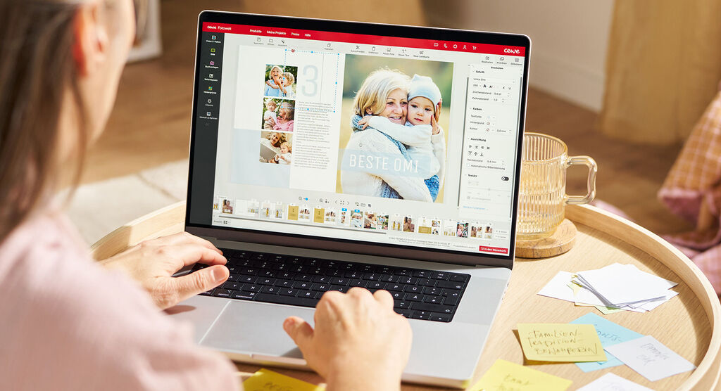 Eine Frau sitzt im Wohnzimmer an einem Couchtisch, auf dem ein Laptop steht. Drumherum sind mehrere bunte Klebezettel ausgebreitet.
