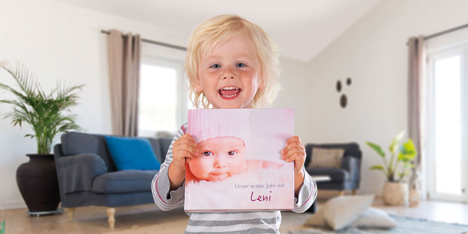 Ein kleines Kind hält ein CEWE Fotobuch mit einem süßen Babyfoto und dem Namen Leni in der Hand.