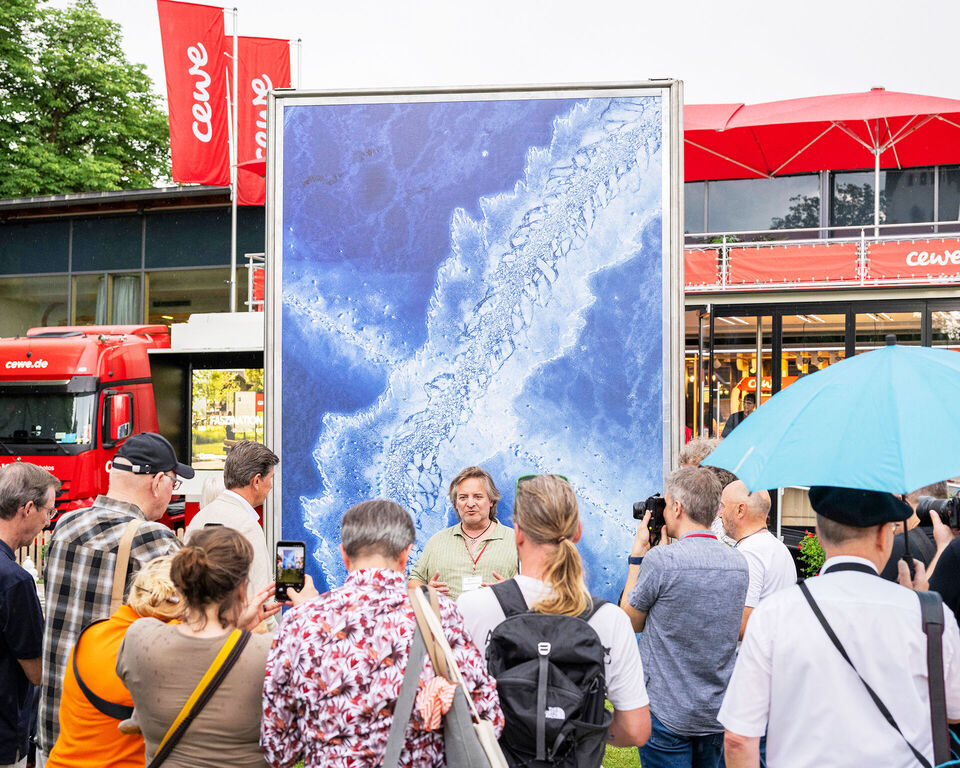 Mehrere Menschen sind vor einer großen Fotoleinwand versammelt. Im Hintergrund steht der CEWE Truck.