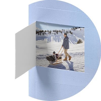 Person zieht Freund auf Schlitten durch verschneite Winterlandschaft