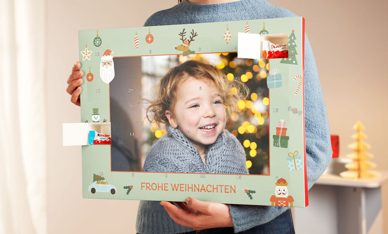 Eine Person hält einen festlichen Bilderrahmen mit Weihnachtsmotiven vor einem unscharfen Hintergrund.