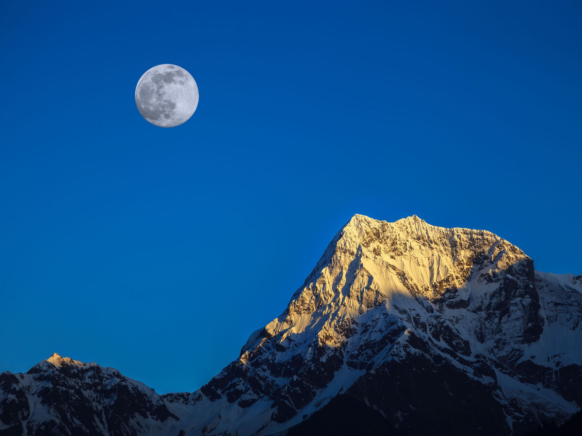 Leuchtender Vollmond am klaren Himmel über sonnigem schneebedecktem Berggipfel