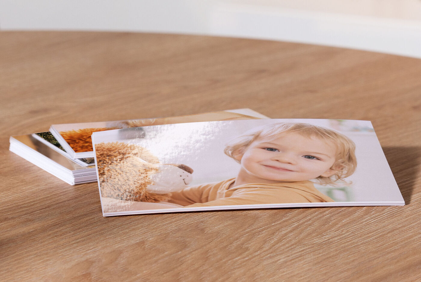 Ein entspanntes Kind mit einem Plüschtier in der Hand, lächelt in die Kamera. Im Hintergrund sind weitere Fotos sichtbar, die auf einem Tisch liegen.
