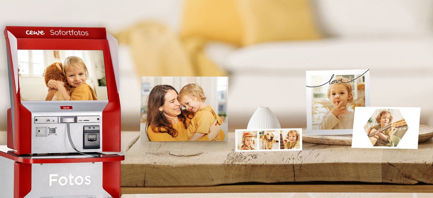 Ein roter Fotoautomat von CEWE zeigt Fotos von lächelnden Kindern auf einem Tisch