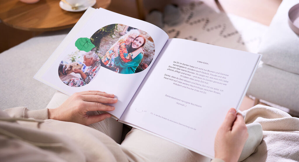 Eine Frau hält in ihren Händen ein aufgeschlagenes CEWE FOTOBUCH, das zwei Fotos und einen abgetippten Brief zeigt.