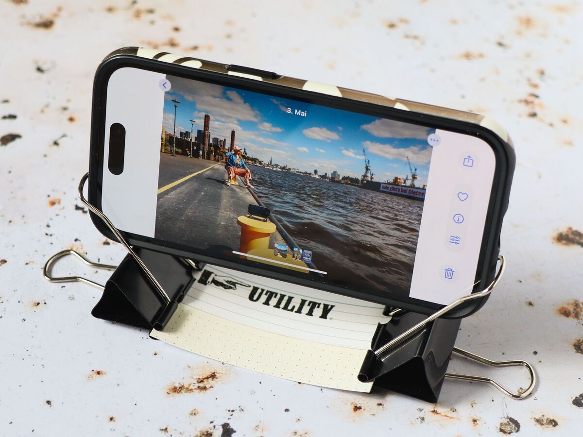 Smartphone auf improvisierter Halterung aus Klammern zeigt ein Foto vom Hafen