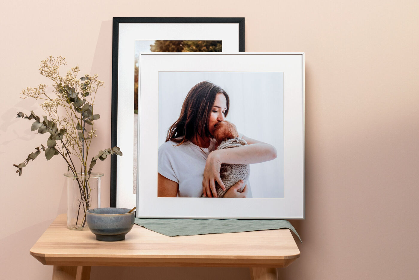 Gerahmtes Foto einer Person mit einem Haustier auf einem Holztisch, umgeben von einer Vase mit Blumen und einem kleinen Geschirr.