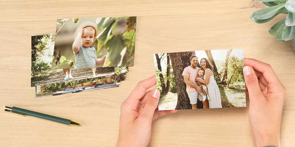 Eine Person hält ein Foto von einem glücklichen Familienmoment in der Hand, umgeben von weiteren Fotos auf einem Tisch