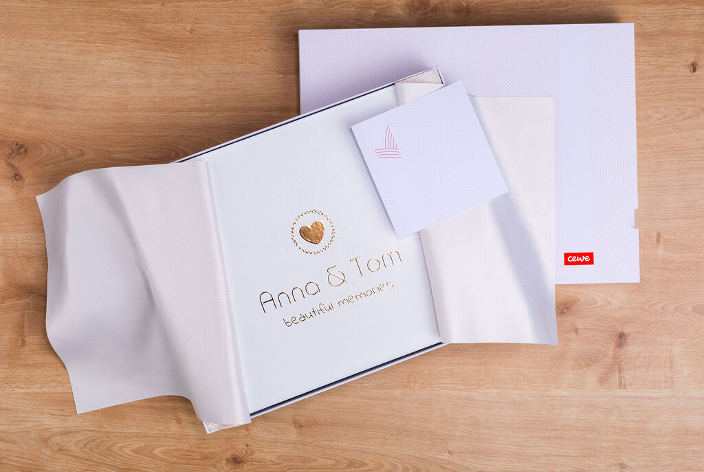 Ein liebevoll gestaltetes CEWE Fotobuch mit dem Namen "Anna & Tom" und einer herzlichen Botschaft, auf einem Holzuntergrund ausgepackt.