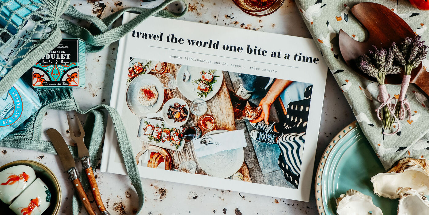 CEWE FOTOBUCH mit Fotos von Speisen; Titel "travel the world one bite a time". Umgeben von maritimen Accessoires.