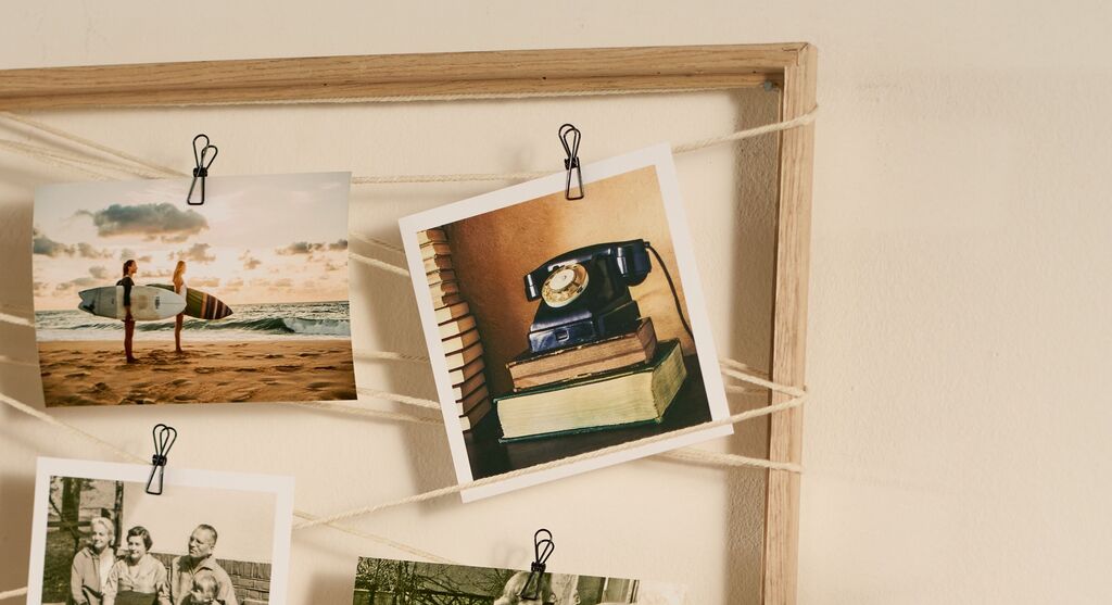 Im Foto sieht man einen hölzernen Rahmen mit gespannten Schnüren, an denen mehrere Fotos mit kleinen Metallklammern befestigt sind