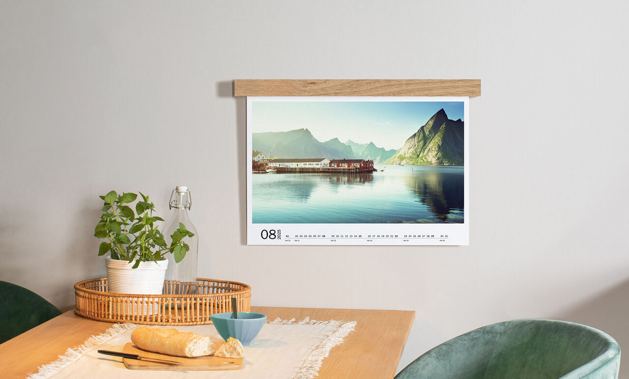 Ein modern gestalteter Kalender hängt an einer Wand über einem Tisch mit einem Korb, Geschirr und einer Pflanze.