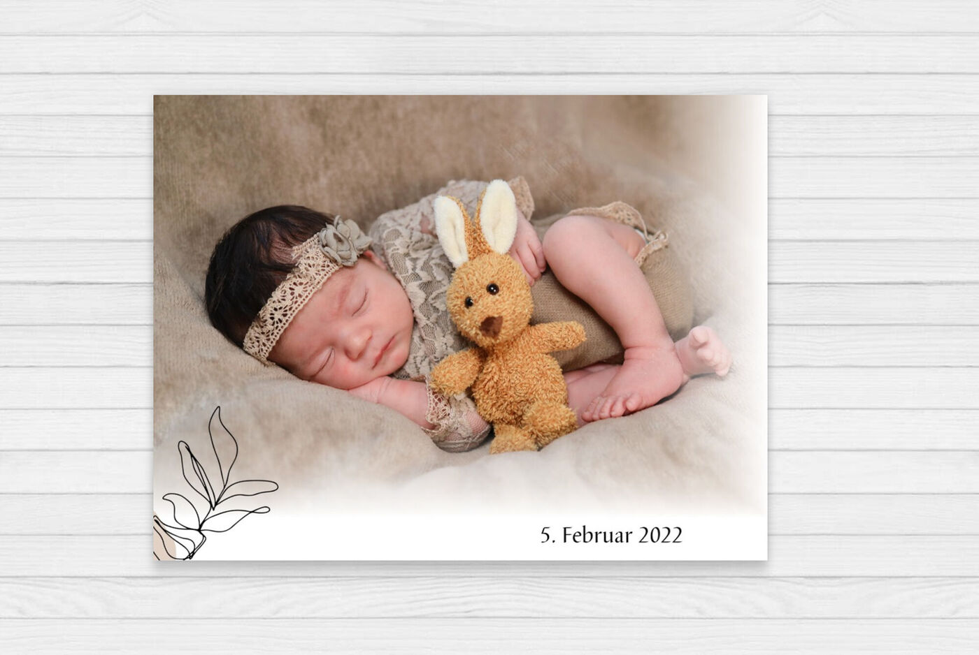 Ein liegendes Baby mit einem braunen Stoffhasen auf einem weichen Untergrund.