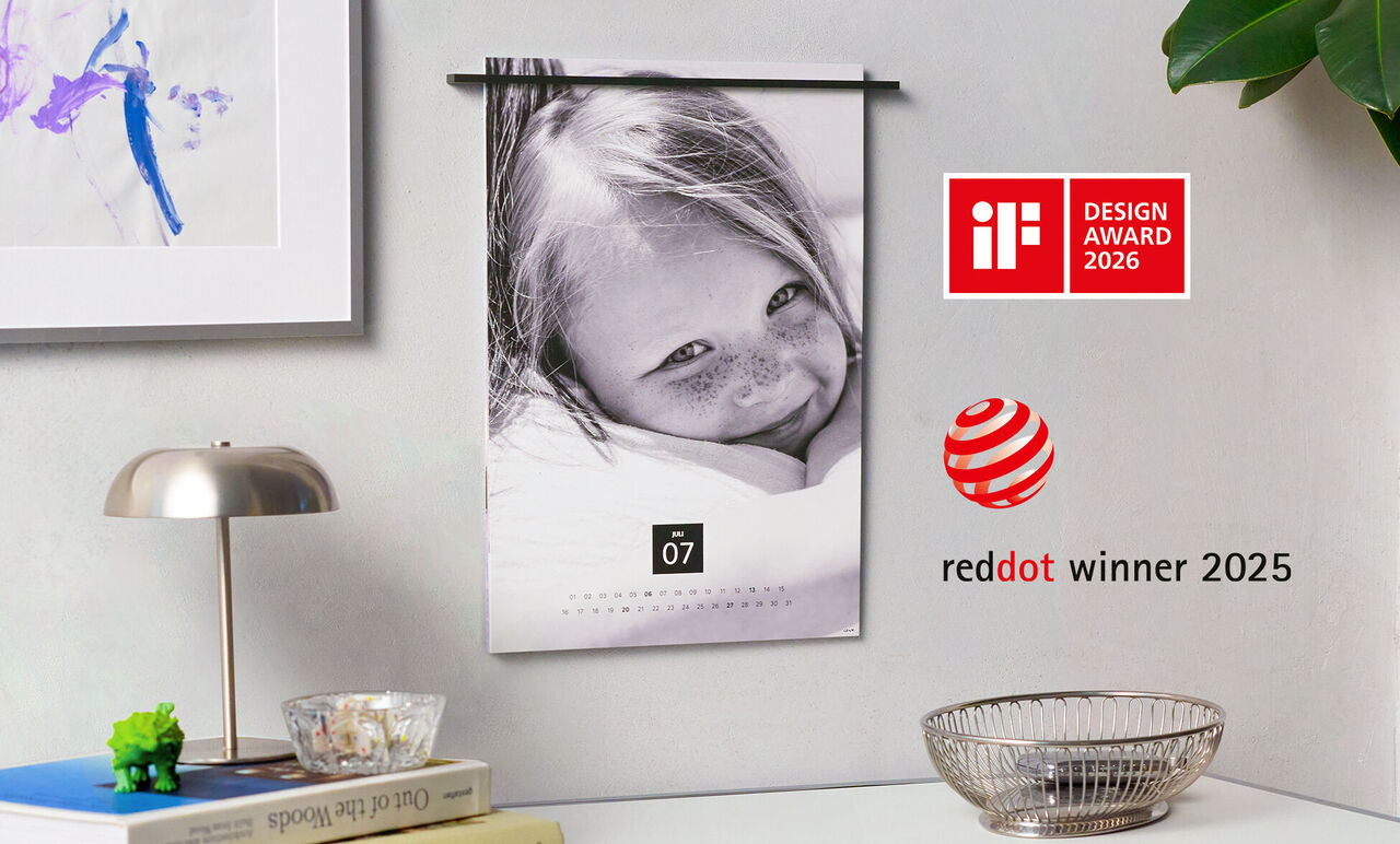 Wandkalender mit einem lächelnden Kind und einem schönen Hintergrund. Der Kalender zeigt den Monat Juli und hat das red dot Design Award Logo.