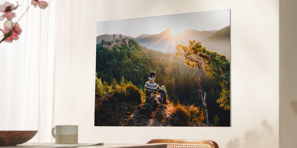 Person mit Pullover schaut auf eine malerische Berglandschaft mit Sonnenstrahlen