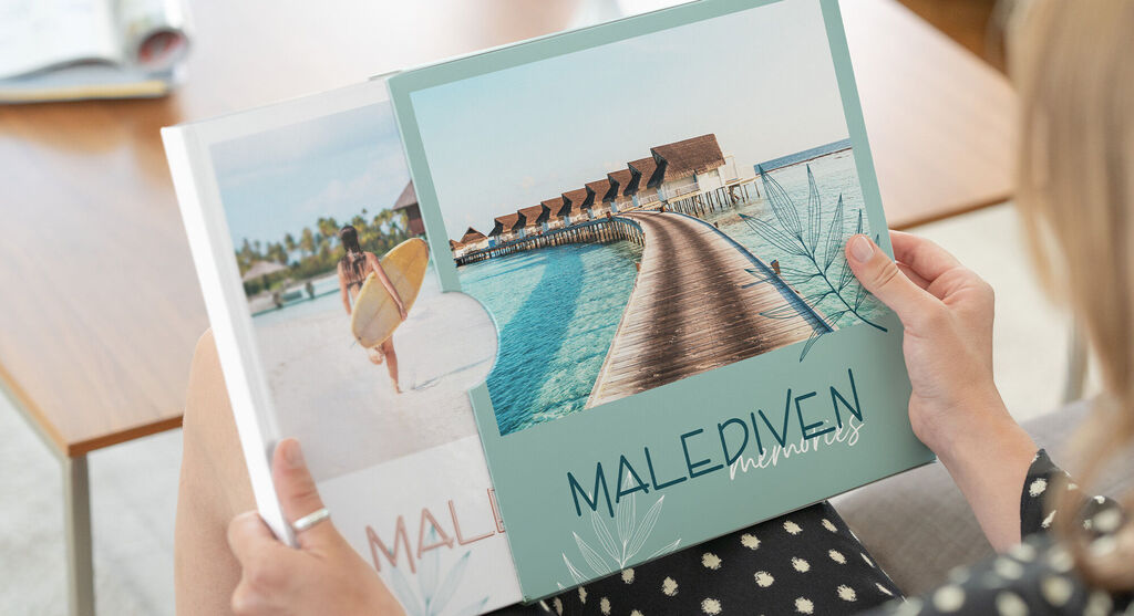 Eine Frau zieht ein Fotobuch vom Malediven-Urlaub aus einem personalisierten Schuber.