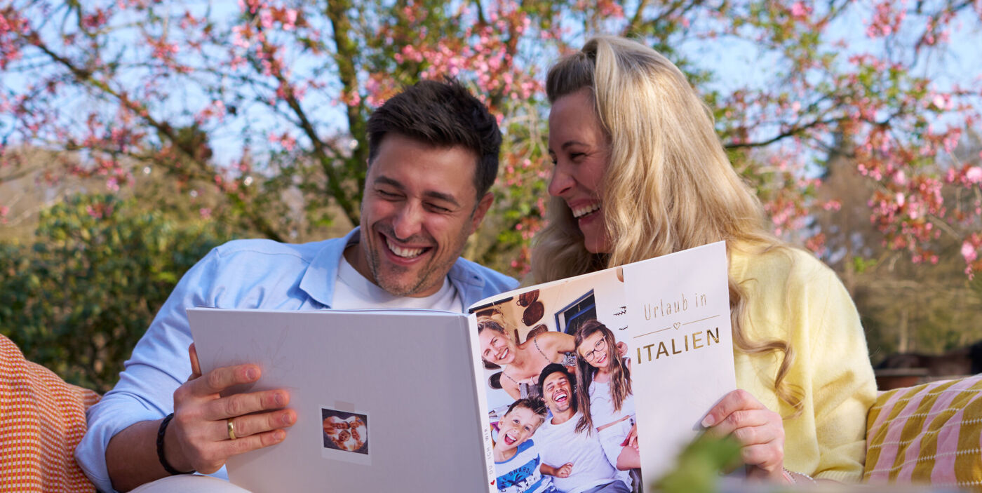 Zwei Personen sitzen draußen und blättern gemeinsam in einem CEWE FOTOBUCH mit Familienbildern.