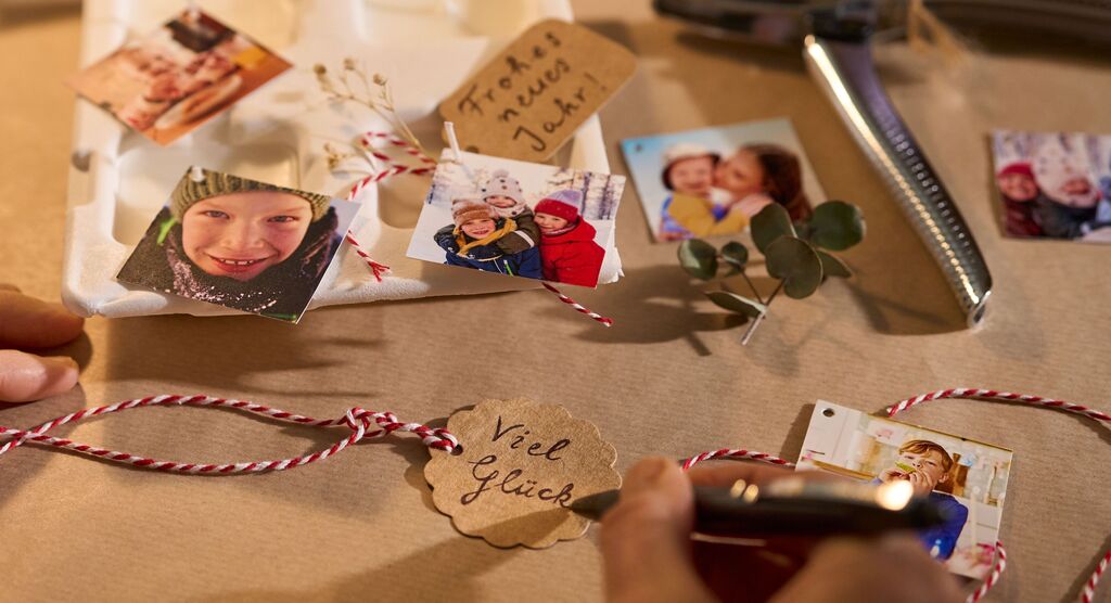Kärtchen mit Fotos, Glückwünschen und Band werden liebevoll für ein Geschenk vorbereitet