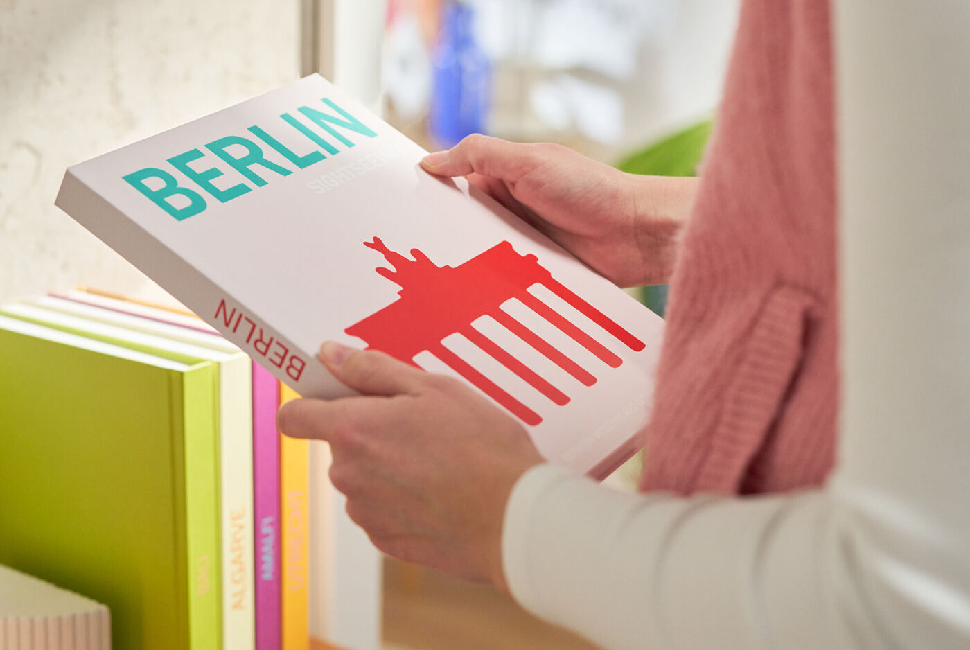 Eine Person hält ein Berlin‑Fotobuch mit einer stilisierten Illustration des Brandenburger Tors auf dem Cover.