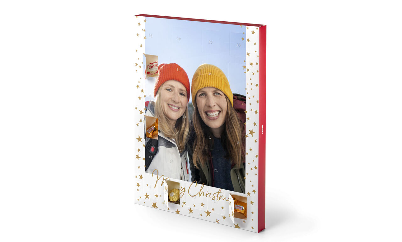  CEWE Fotobuch mit weihnachtlichem Design, zwei Personen halten es. Auf dem Cover sind goldene Sterne und der Schriftzug „Merry Christmas“.