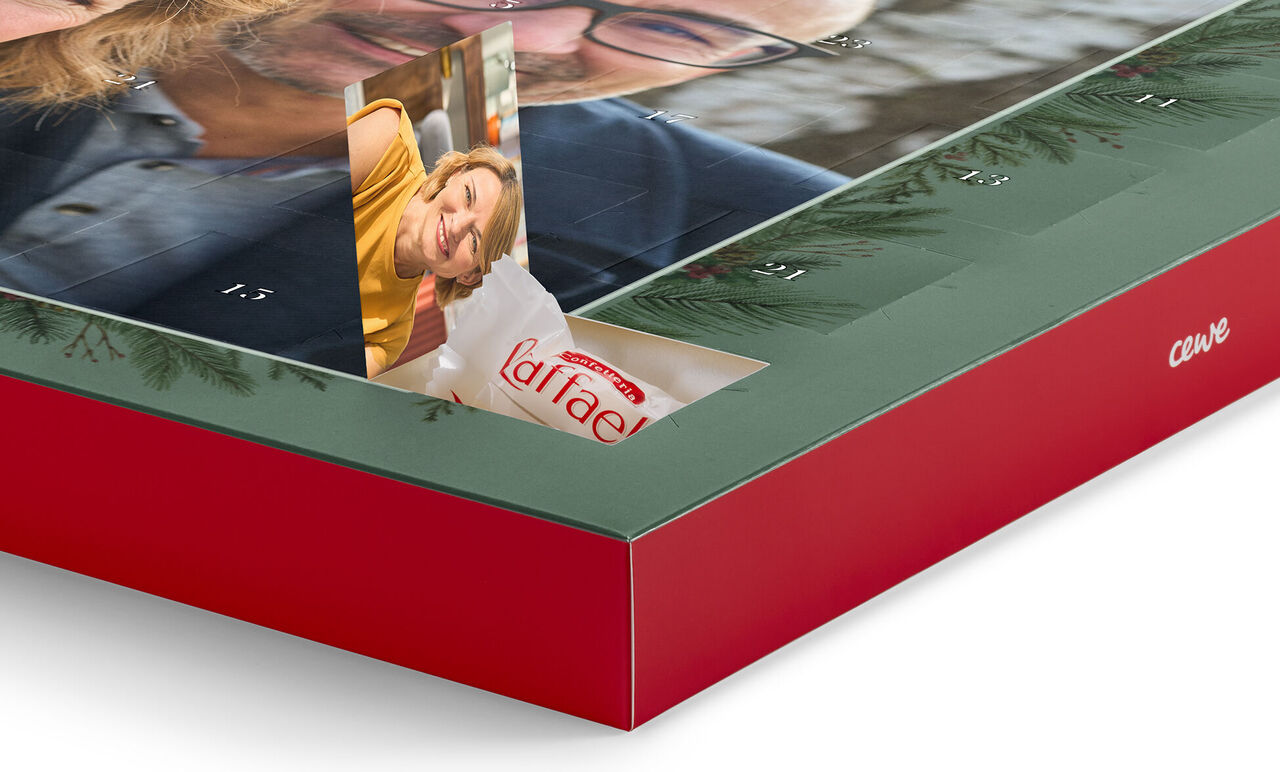 Ein geöffneter CEWE Fotokalender zeigt ein fröhliches Bild von einer Frau, die lächelt, aus einer Klappe. Der Kalender hat einen roten Rand und weihnachtliche Motive.