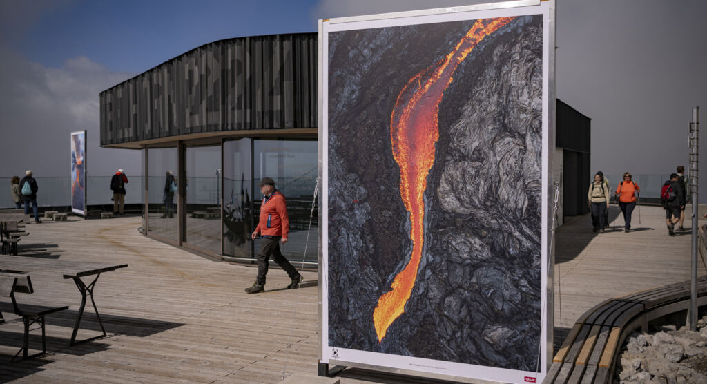 Auf einer belebten Terrasse steht ein großes Bild, das einen Vulkanausbruch zeigt.