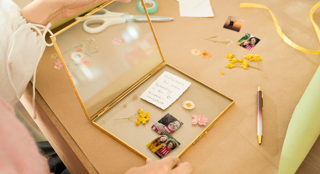 Eine Person gestaltet kreativ ein Erinnerungsglas mit Fotos und Trockenblumen