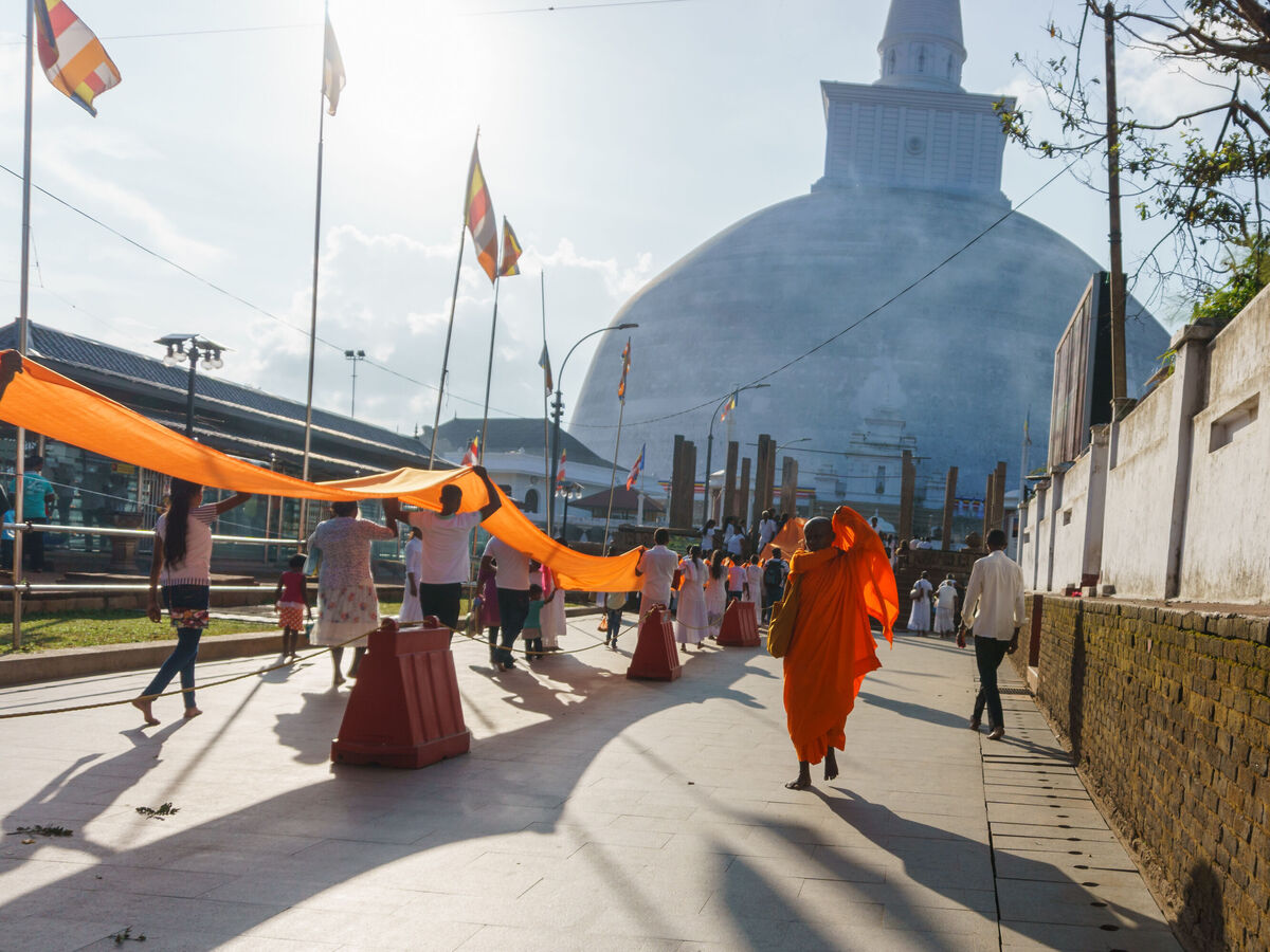Mönche und Menschen bei einem Fest mit orangefarbenen Stoffbahnen vor einem großen weißen Stupa in Nepal